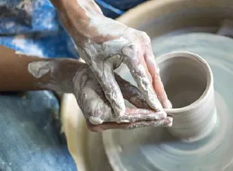 a pair of hands covered in clay creating a piece of pottery
